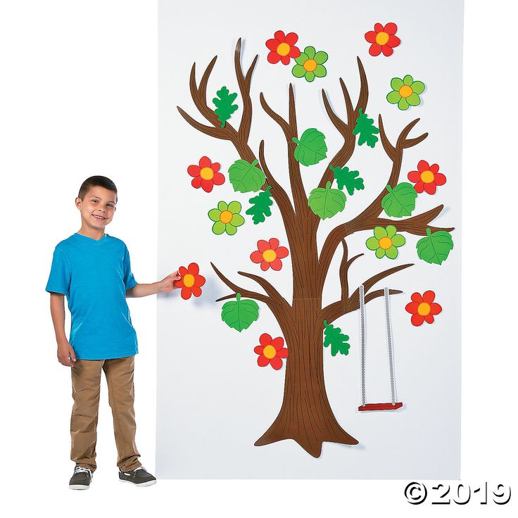 a young boy standing next to a tree cut out of paper with flowers on it