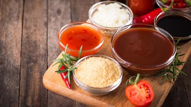 various sauces and condiments on a cutting board with tomatoes, peppers, rice