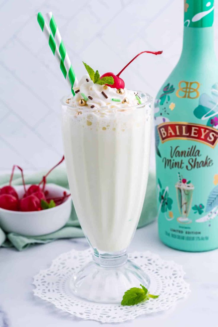 a milkshake with whipped cream and cherries on the rim next to a bottle of bailey's vanilla mint shake