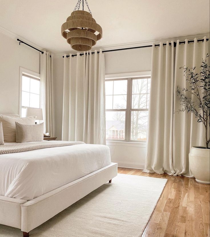 a white bed sitting in a bedroom next to a window with curtains on both sides