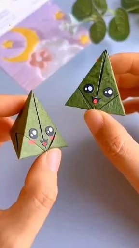 two hands holding origami pieces with eyes and nose on them, one is green