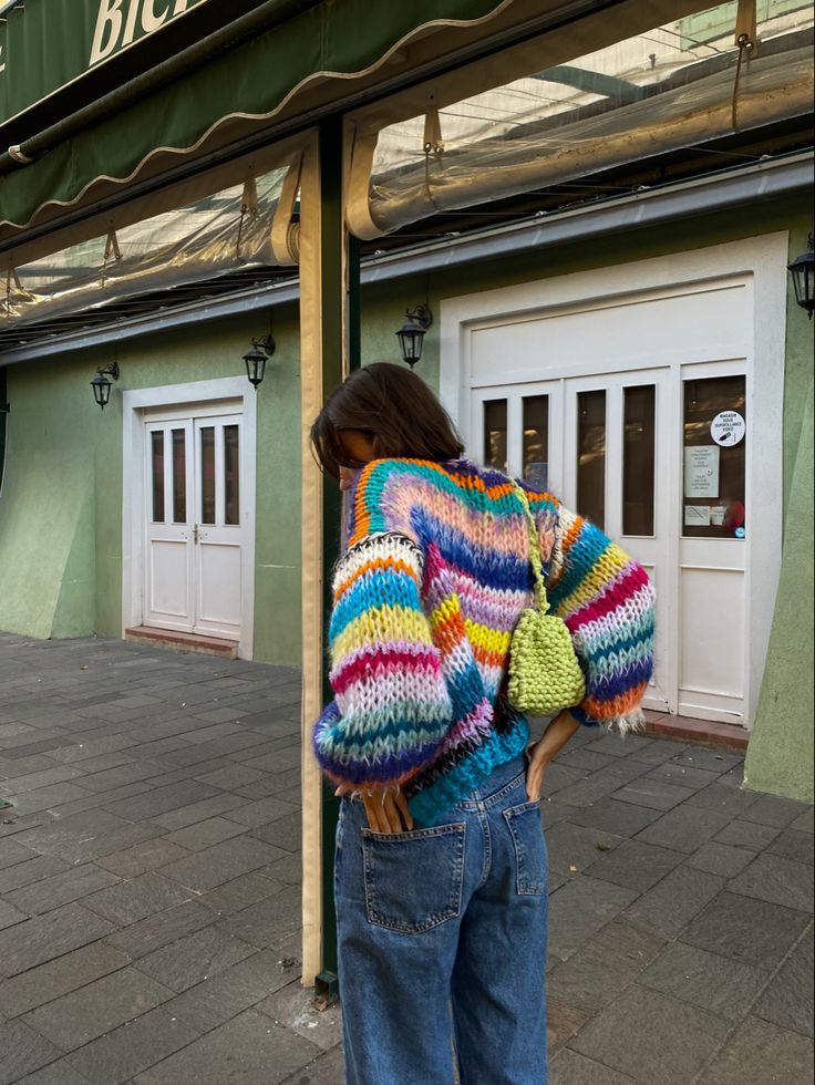 a woman is standing on the sidewalk in front of a building wearing a colorful sweater