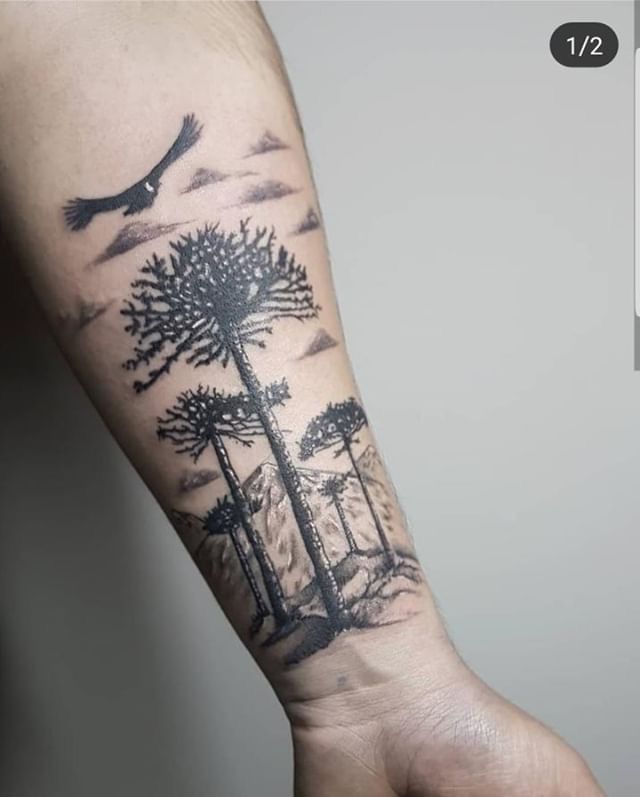 a person with a tattoo on their arm holding a bird in the sky and trees