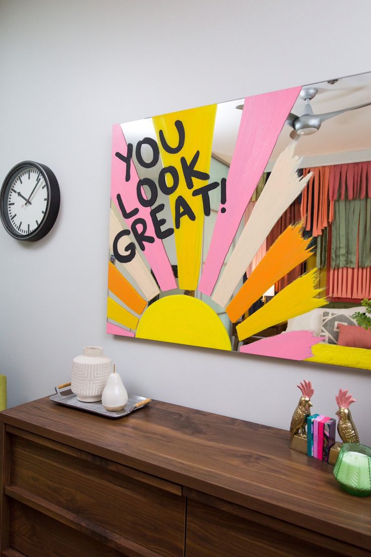 there is a clock on the wall next to a dresser with an art work on it