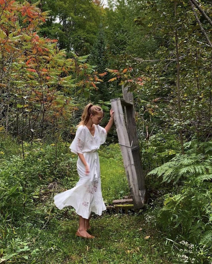 a woman in a white dress leaning against a wooden post