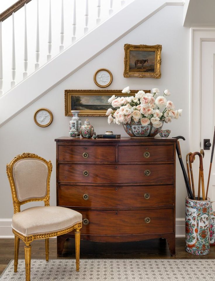 a room with a chair, vases and flowers on the dresser next to stairs