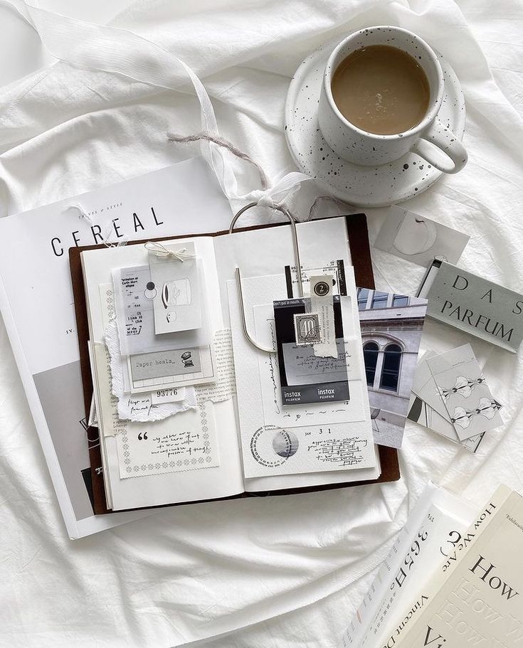 an open book sitting on top of a white bed next to a cup of coffee