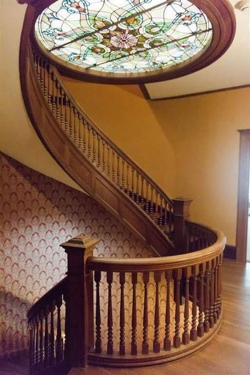 a spiral staircase in front of a stained glass window with wooden handrails and banister