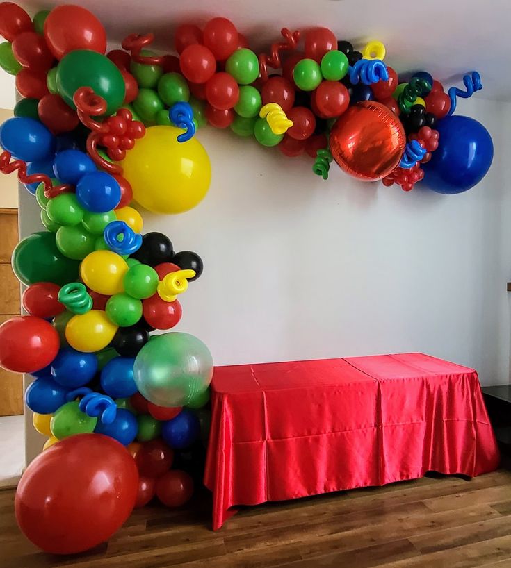 a room filled with balloons and a table covered in a red cloth under the balloon arch