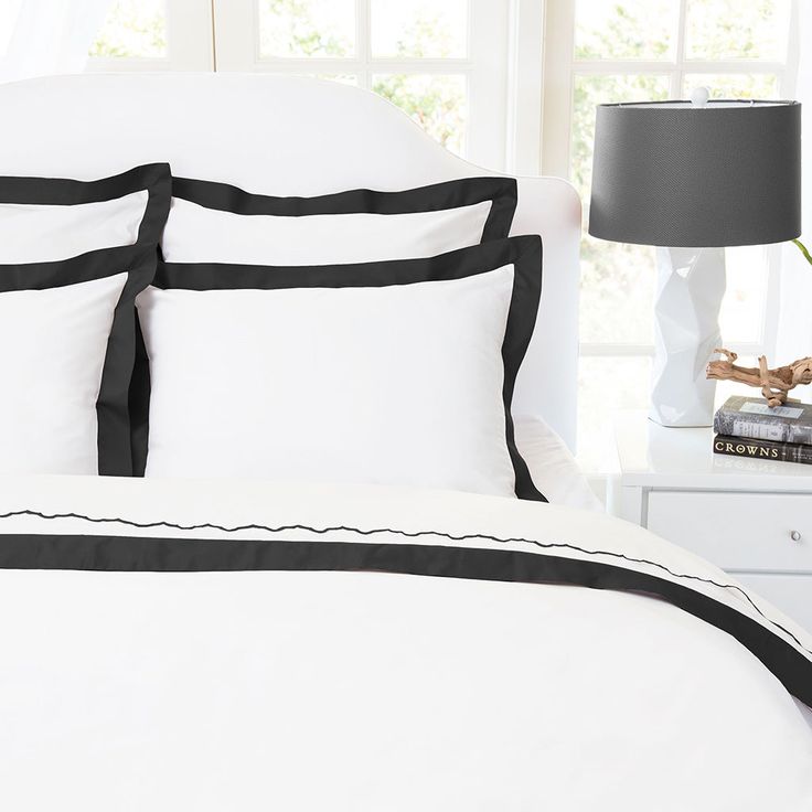 a white bed with black trimmings and two lamps on the nightstand next to it