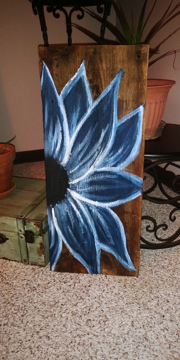 a painted wooden block with a blue flower on it next to a potted plant