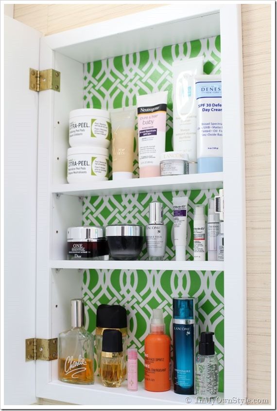 an open medicine cabinet filled with cosmetics and skin care products in front of a wallpapered background