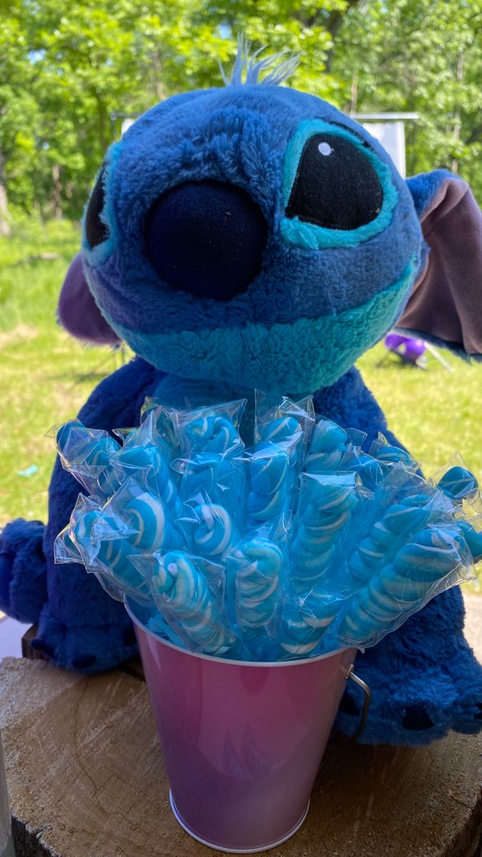 a blue stuffed animal sitting on top of a tree stump next to a pink cup