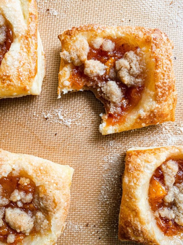 four small pastries on a baking sheet with powdered sugar and jelly toppings