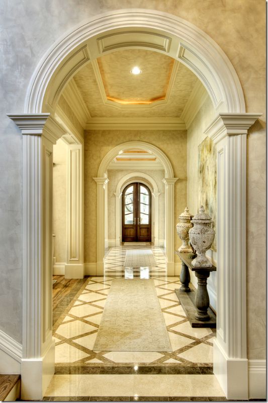 an archway leading to a large foyer with marble floors and columns on either side, flanked by two urns