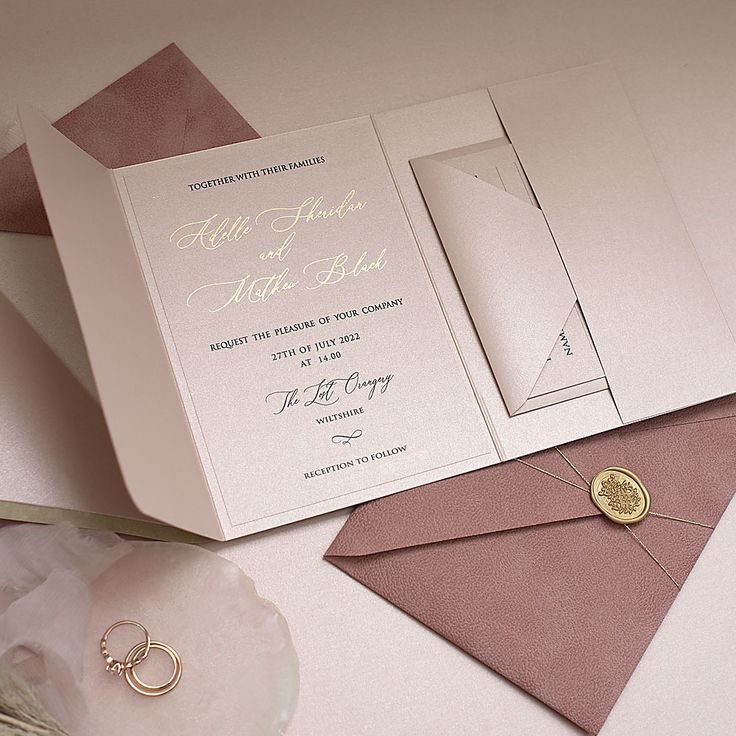 an open wedding card with two rings on it and a flower in the middle next to it