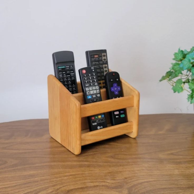 four remote controls in a wooden holder on a table next to a potted plant