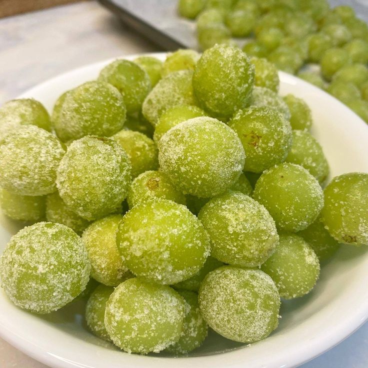 a white bowl filled with green powdered sugar coated grapes on top of a counter