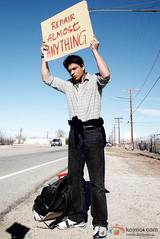 a man holding up a sign while standing on the side of the road with luggage