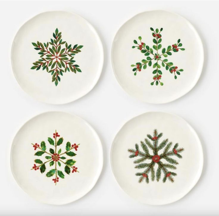 four white plates with green and red designs on the rims, all decorated with holly leaves