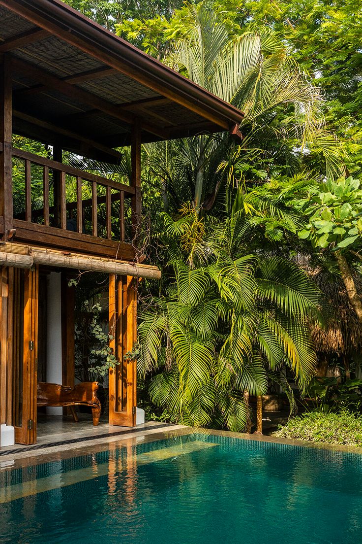 a house with a pool in front of it surrounded by trees and greenery on the other side