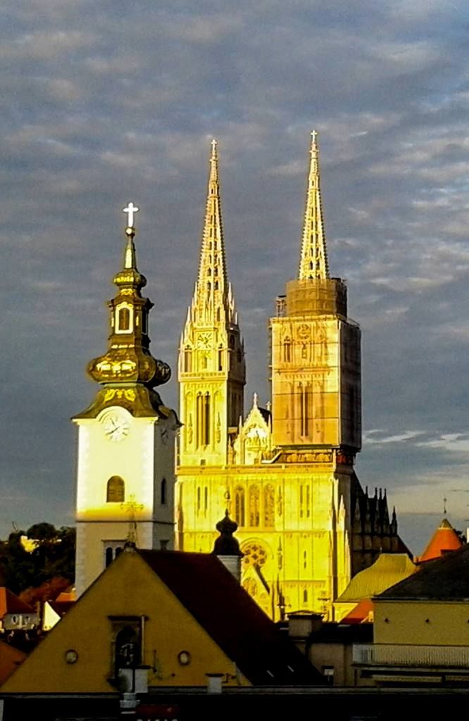 the cathedrals are lit up at night with clouds in the sky above them and buildings below