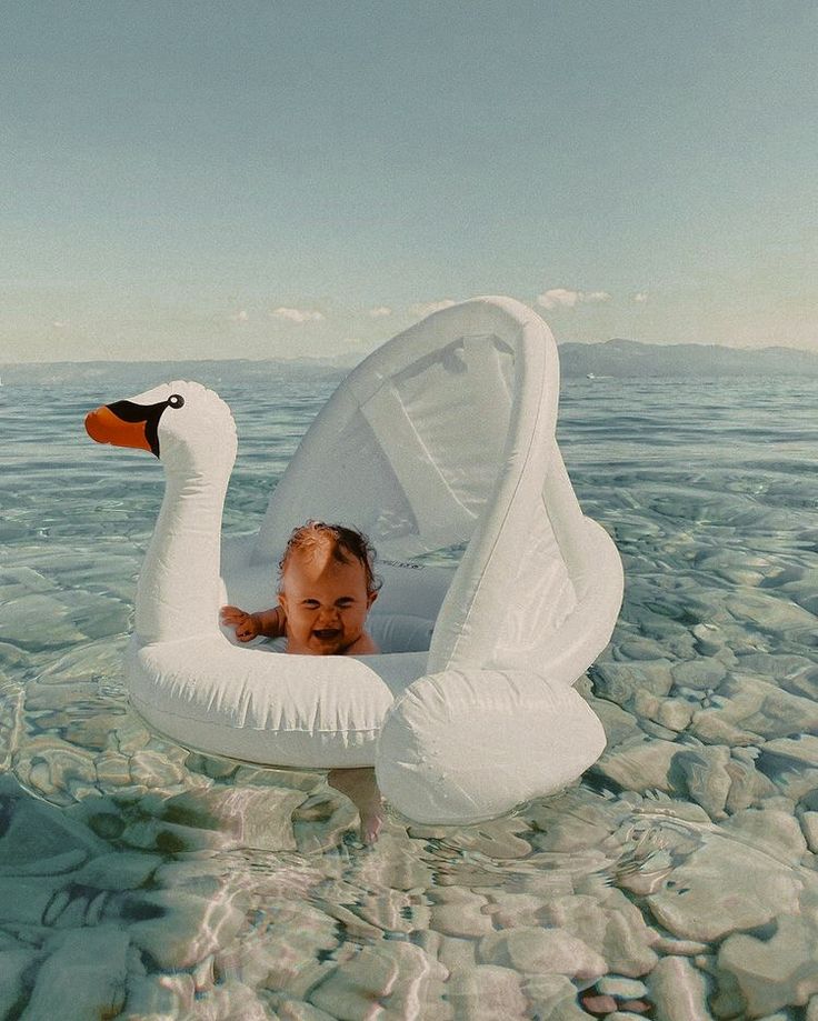 a baby in an inflatable swan floatie floating on the water with its head sticking out