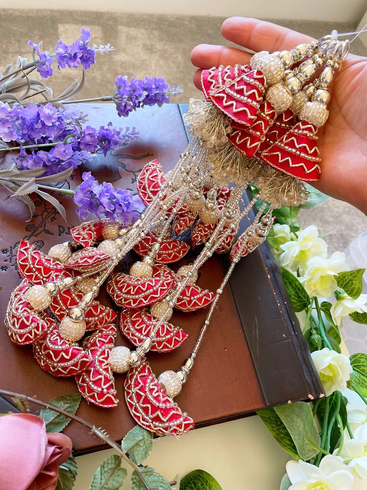 a hand is holding some red and white decorations with flowers in the background on a table