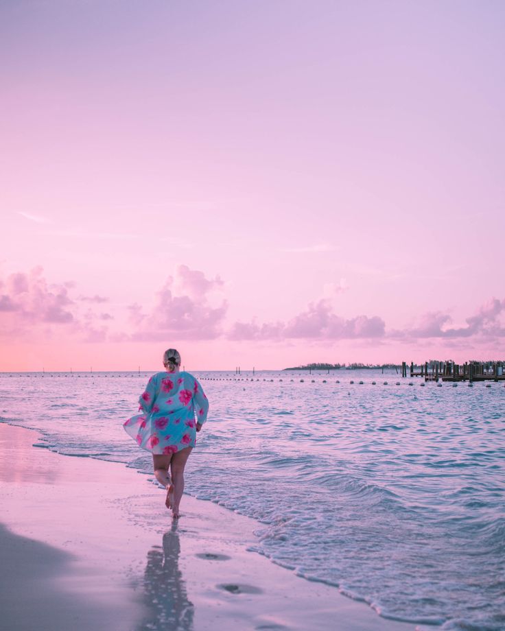 a woman walking on the beach at sunset