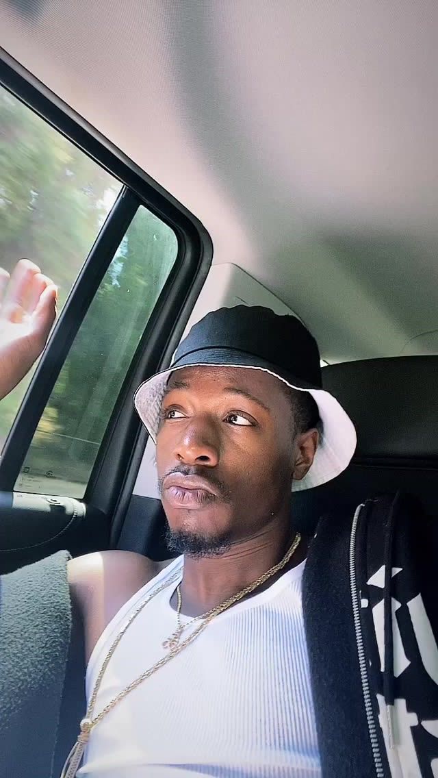 a man sitting in the back seat of a car wearing a hat and holding his hand up