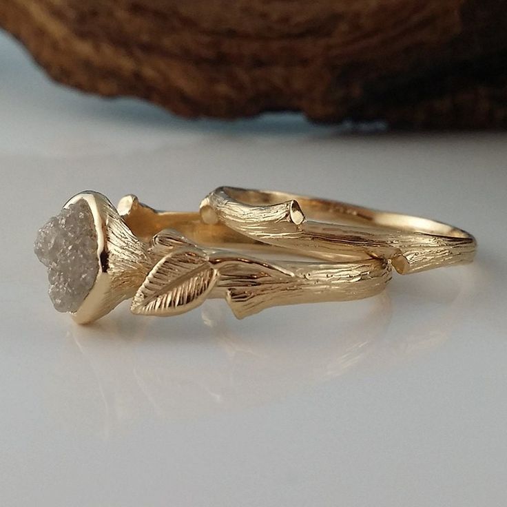 two gold rings with leaves on them sitting on a white surface next to a piece of wood