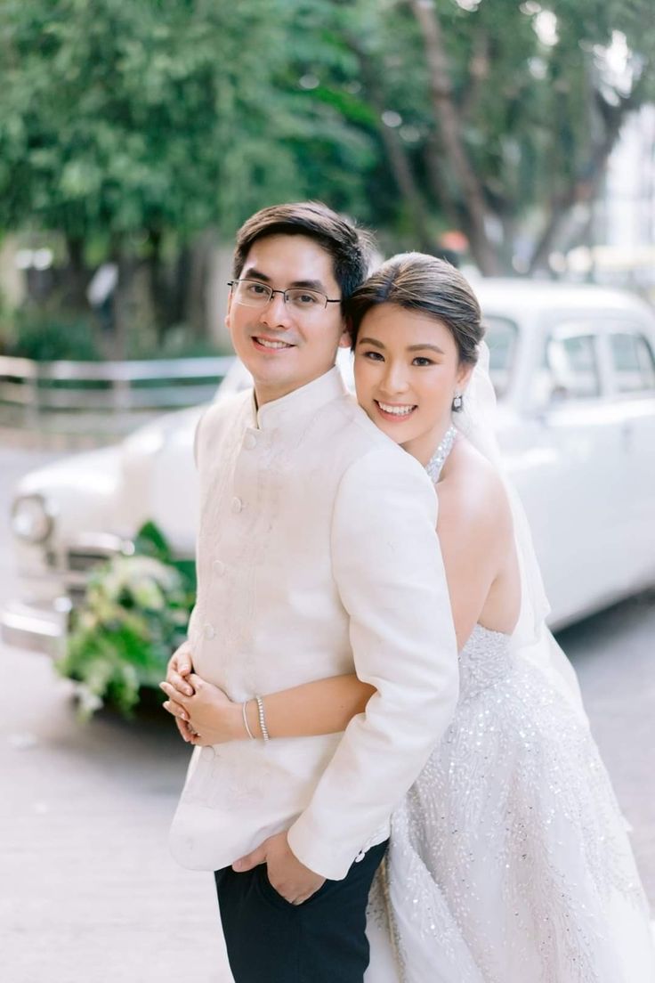 a man and woman standing next to each other in front of a white vintage car