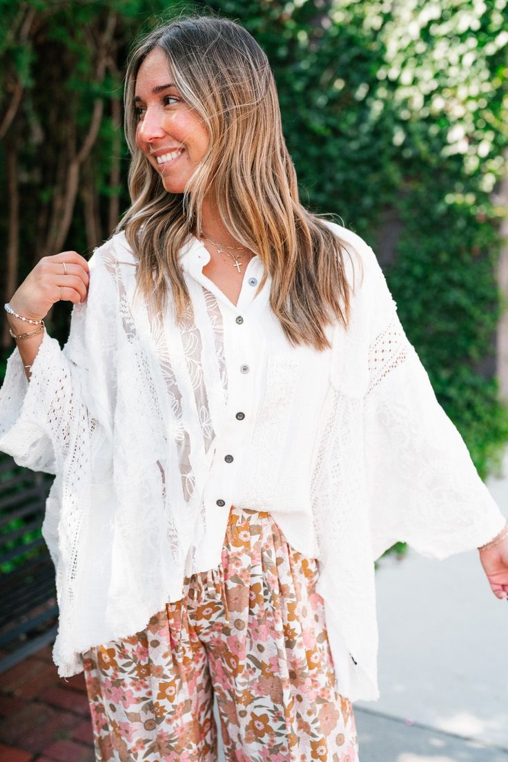 The Lakelyn Lace Ivory Button Up Top is a beautifully crafted, off-white lace and gauze blouse that exudes a romantic, bohemian vibe. The top features a delicate mix of lace and textured fabric, creating a soft and airy look perfect for layering. It has a button-down front with small, dark buttons that add a subtle contrast to the light fabric. The collar is slightly frayed, contributing to its relaxed and effortless style. The sleeves are voluminous and made entirely of intricate lace, adding a Lace Blouse With Crochet Trim For Brunch, Bohemian Button-up Blouse For Vacation, White Crochet Lace Top For Day Out, Bohemian Button-up Blouse For Day Out, White Lace Top With Crochet Trim, White Feminine Lace Top With Crochet Trim, White Feminine Crochet Top For Brunch, White Lace Top With Crochet Trim For Daywear, White Lace Top With Patchwork For Day Out