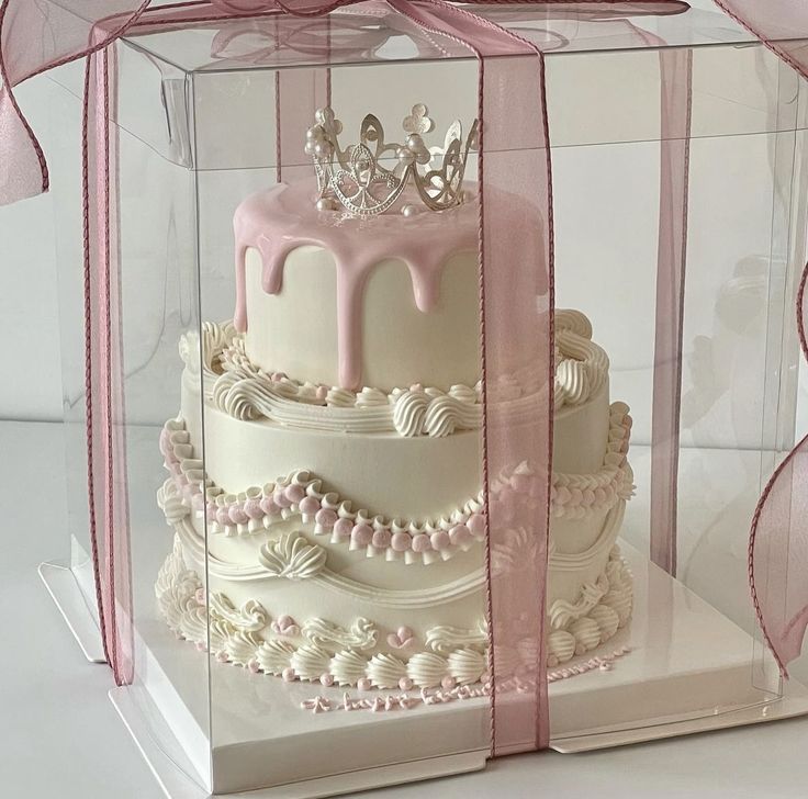 a three tiered cake in a clear box with pink ribbon and bow on top