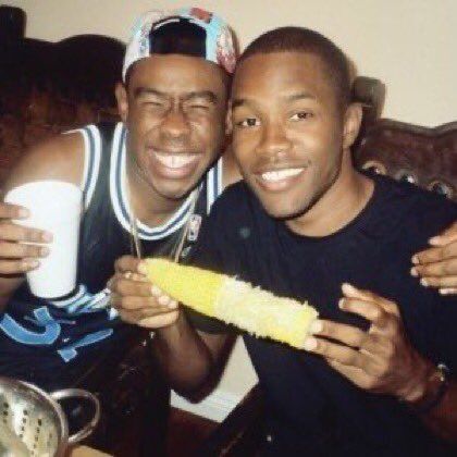 two men sitting next to each other holding corn on the cob