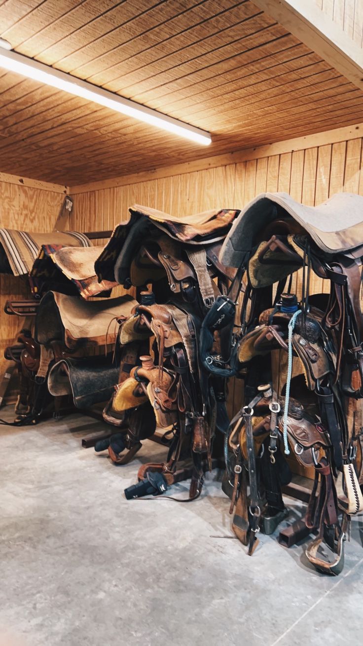 several different types of saddles stacked on top of each other in a room with wood paneling