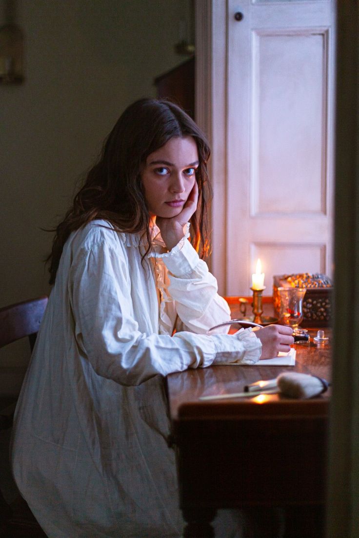 a woman sitting at a table with a candle in front of her and looking off to the side