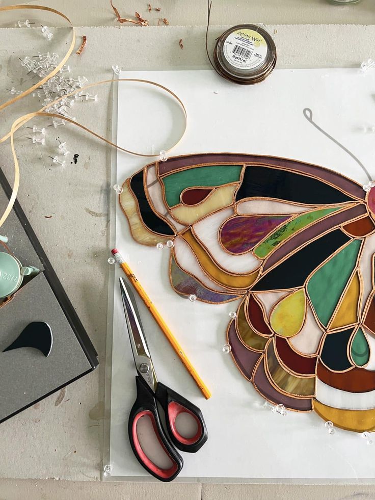 a butterfly made out of stained glass sitting on top of a table next to scissors