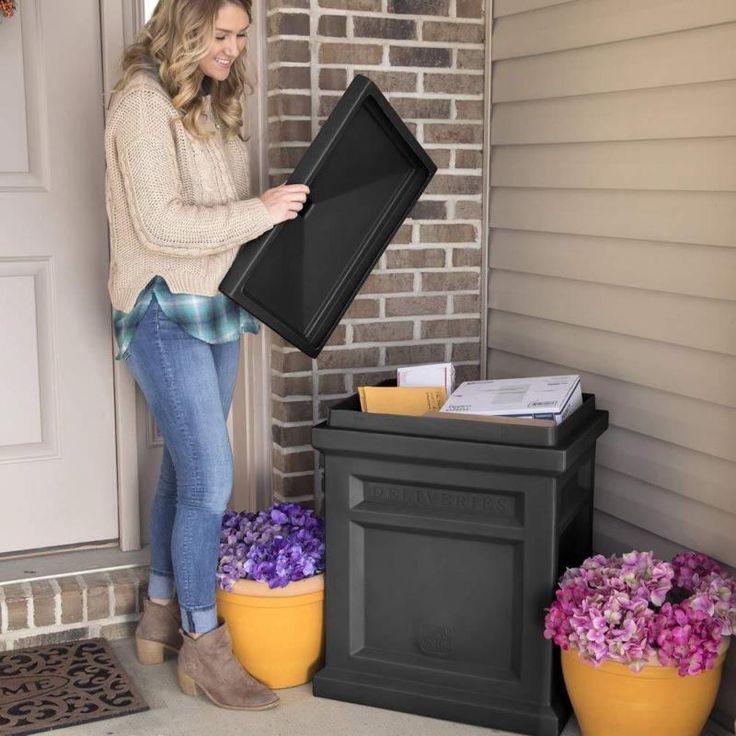 a woman holding up a large black box in front of a door with purple flowers