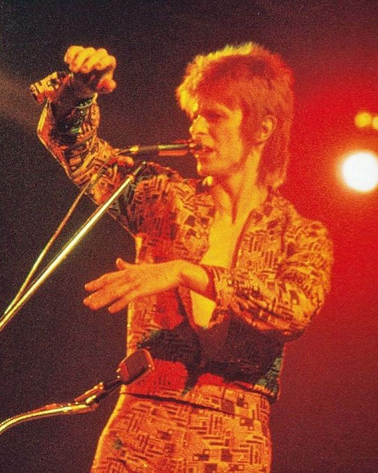 a man standing in front of a microphone on stage with his hands out to the side