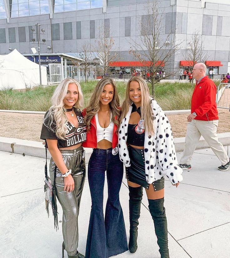 three beautiful women standing next to each other in front of a building with people walking by