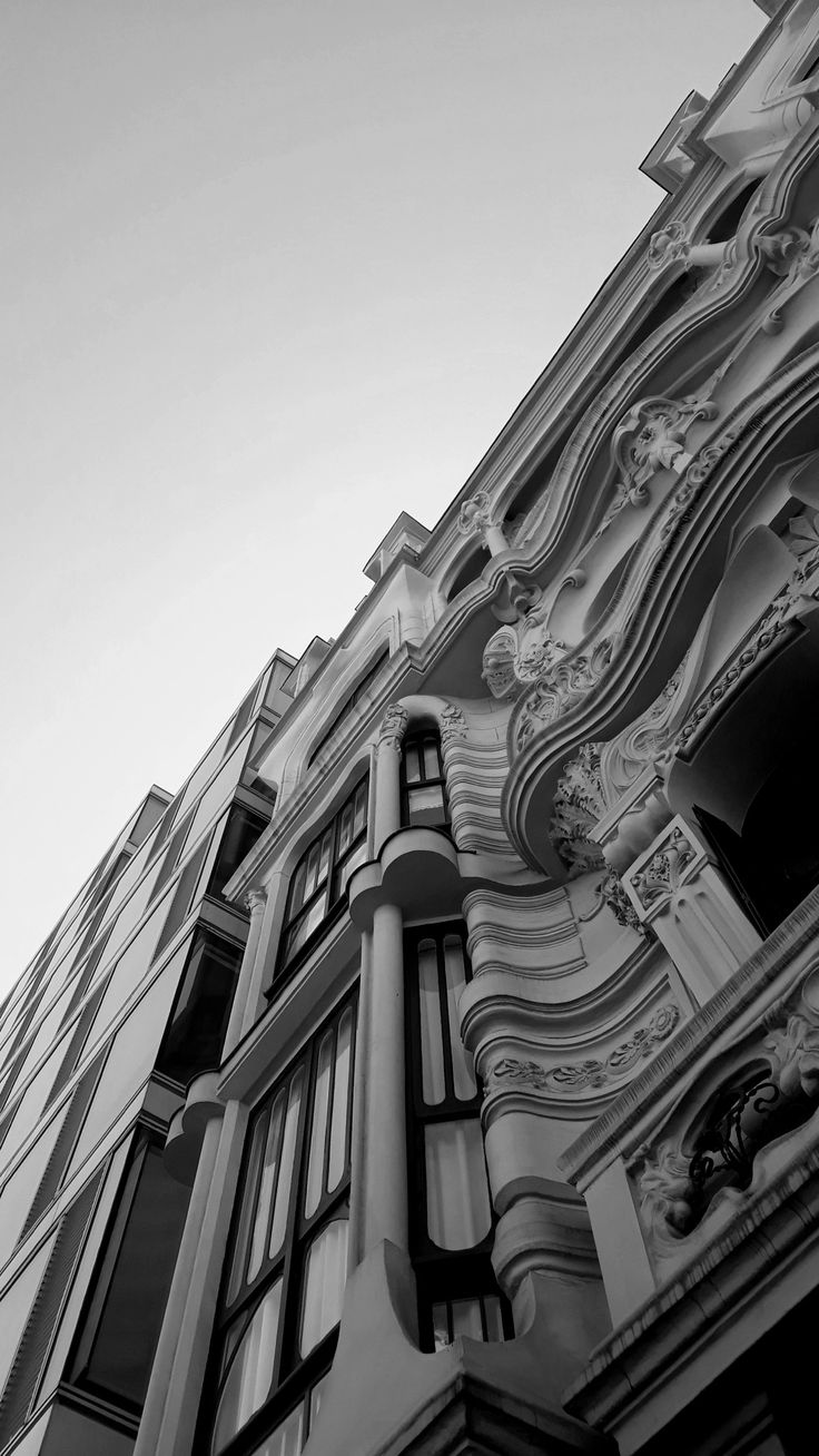 a black and white photo of a tall building with windows on the top floor, looking up at the sky