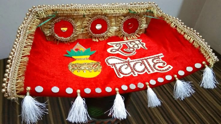 a red and gold purse with tassels on it sitting on a table next to a wall