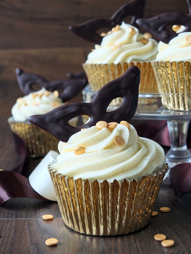 cupcakes with white frosting and chocolate decorations on top, sitting on a table