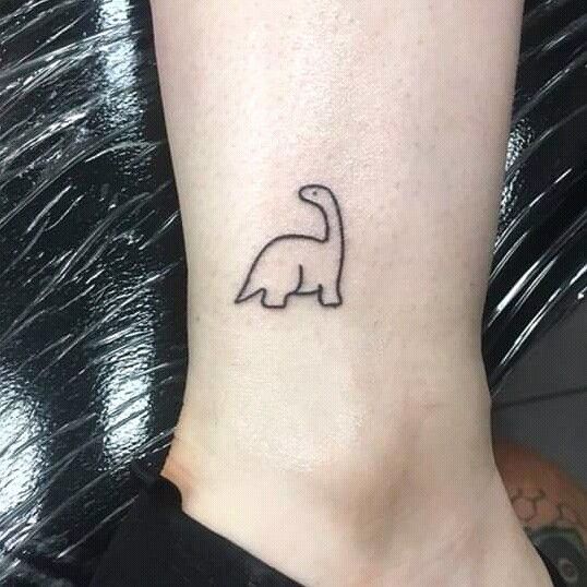 a small tattoo on the ankle of a woman's foot that has a dinosaur drawn on it