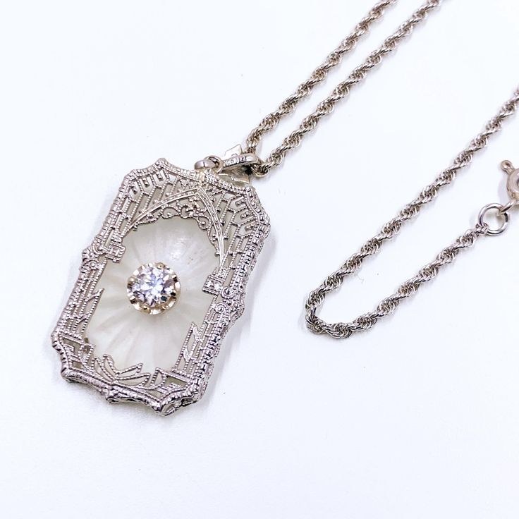 This stunning Art Deco pendant showcases the timeless beauty of camphor glass, set in intricate filigree work. The large center diamond accent in its buttercup setting adds a touch of luxury. Crafted by Esemco, a renowned jewelry maker founded in 1906 in Newark, NJ, this piece is a true collector's item. A 14k white gold chain completes the elegant ensemble. This piece exudes vintage style and sophistication. Perfect for Weddings, anniversaries, or other formal events or just add a a touch of ti Newark Nj, White Gold Chain, Art Deco Pendant, Filigree Pendant, Locket Charms, Jewelry Maker, Glass Set, Timeless Beauty, Pendant Necklaces