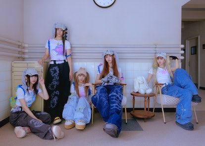 four young women sitting on chairs in front of a wall with a clock above them