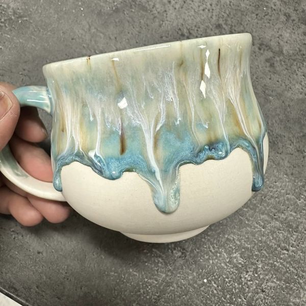 a hand holding a coffee cup with blue and green swirls on the outside of it