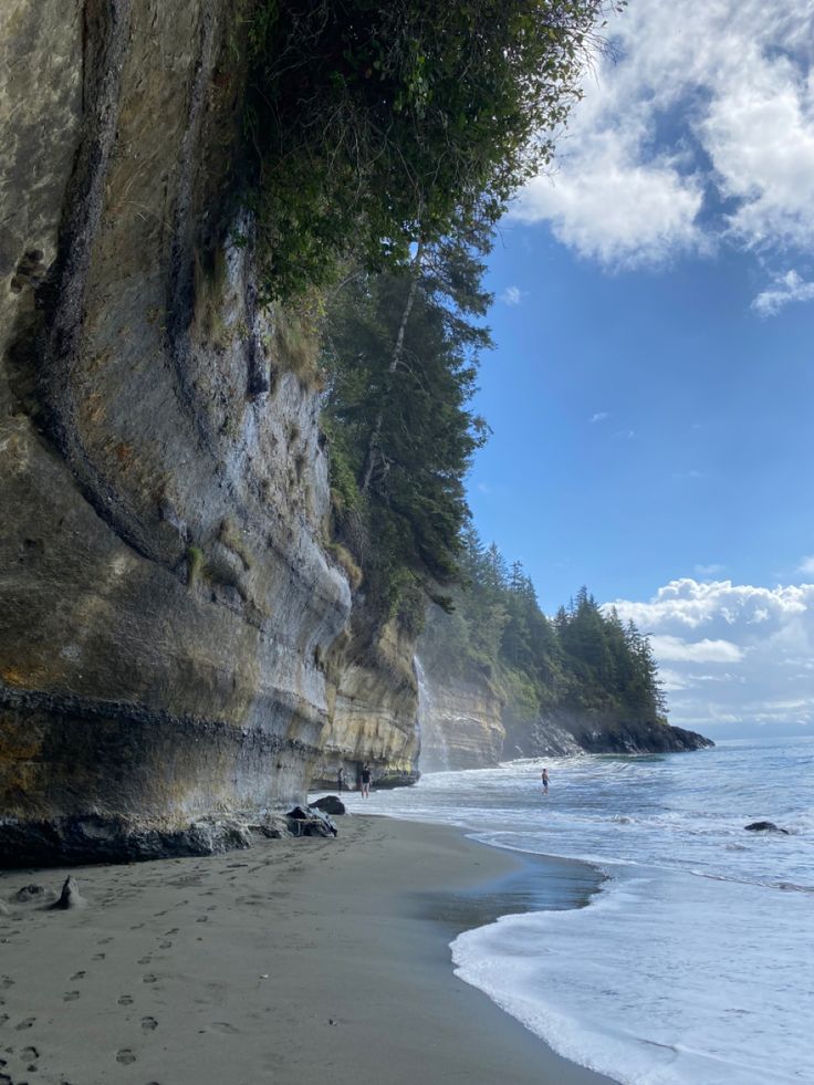 a person walking along the edge of a cliff on a beach next to the ocean