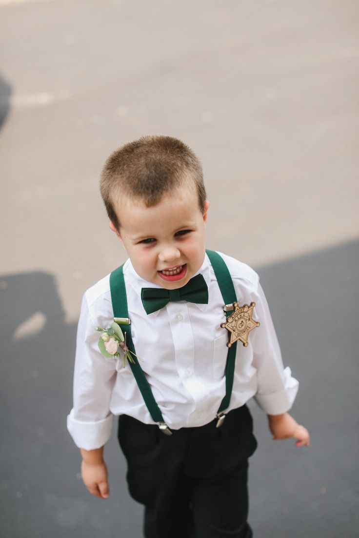 a young boy in a white shirt and green suspenders is smiling at the camera